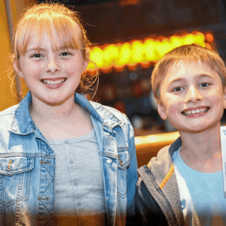 An image of two children looking excited, holding their theatre tickets up.