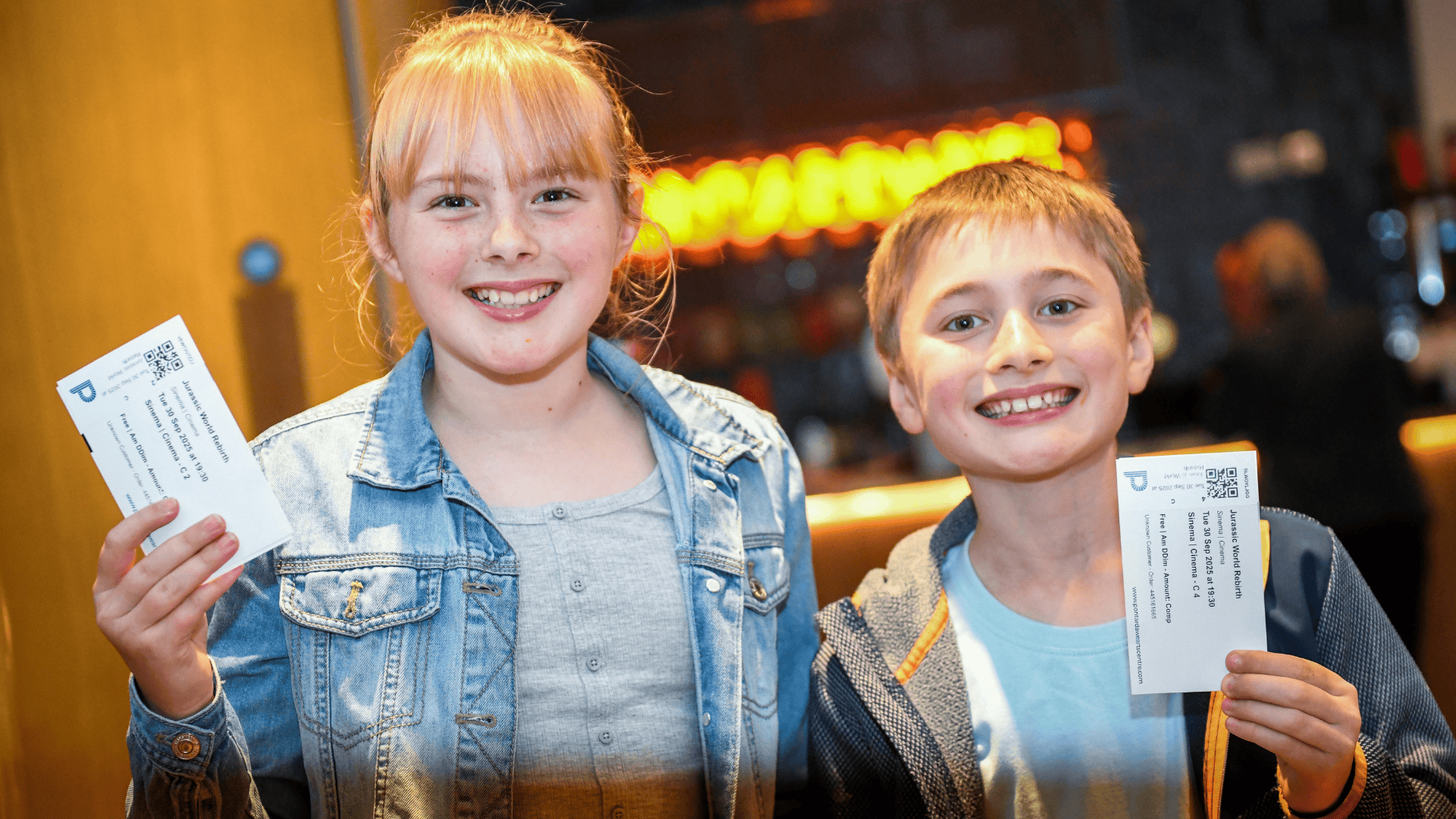 An image of two children looking excited, holding their theatre tickets up.